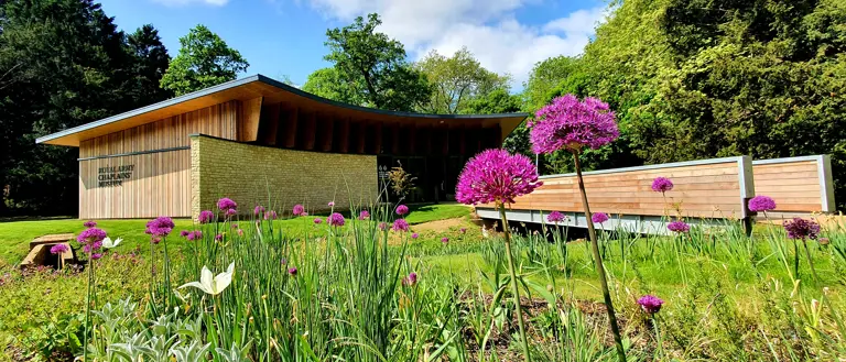 A museum is pictured from the exterior, purple flowers are present in the foreground.
