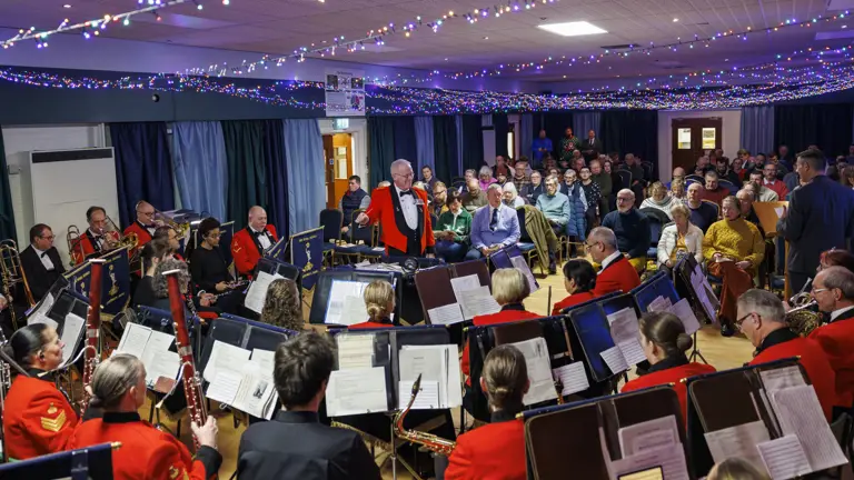 Indoor concert with a seated audience watching a band in red uniforms performing under string lights.