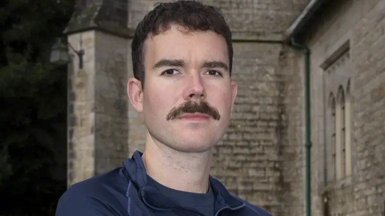 Portrait of a soldier seen in a plain top with the royal army chaplain cap badge on the chest posing for a photo