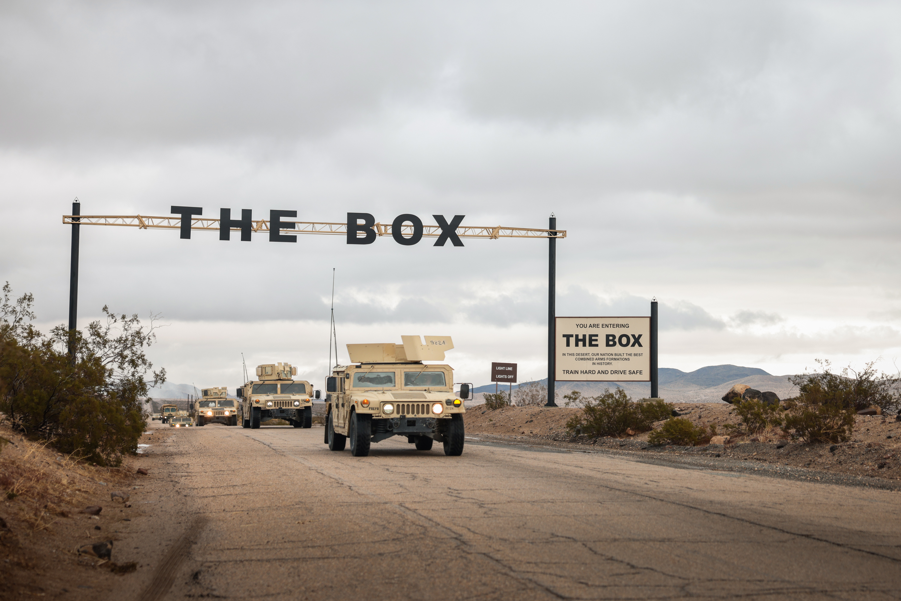 Sand coloured American vehicles drive under a sign that says 
