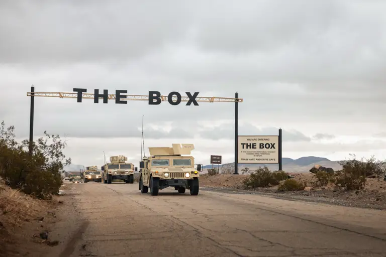 Sand coloured American vehicles drive under a sign that says