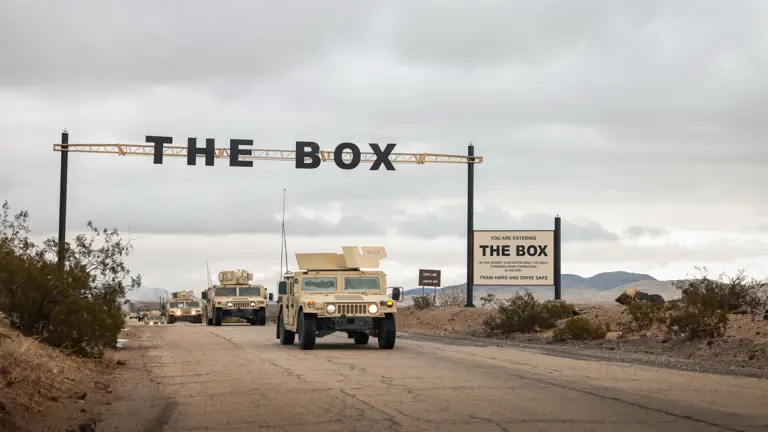 Sand coloured American vehicles drive under a sign that says