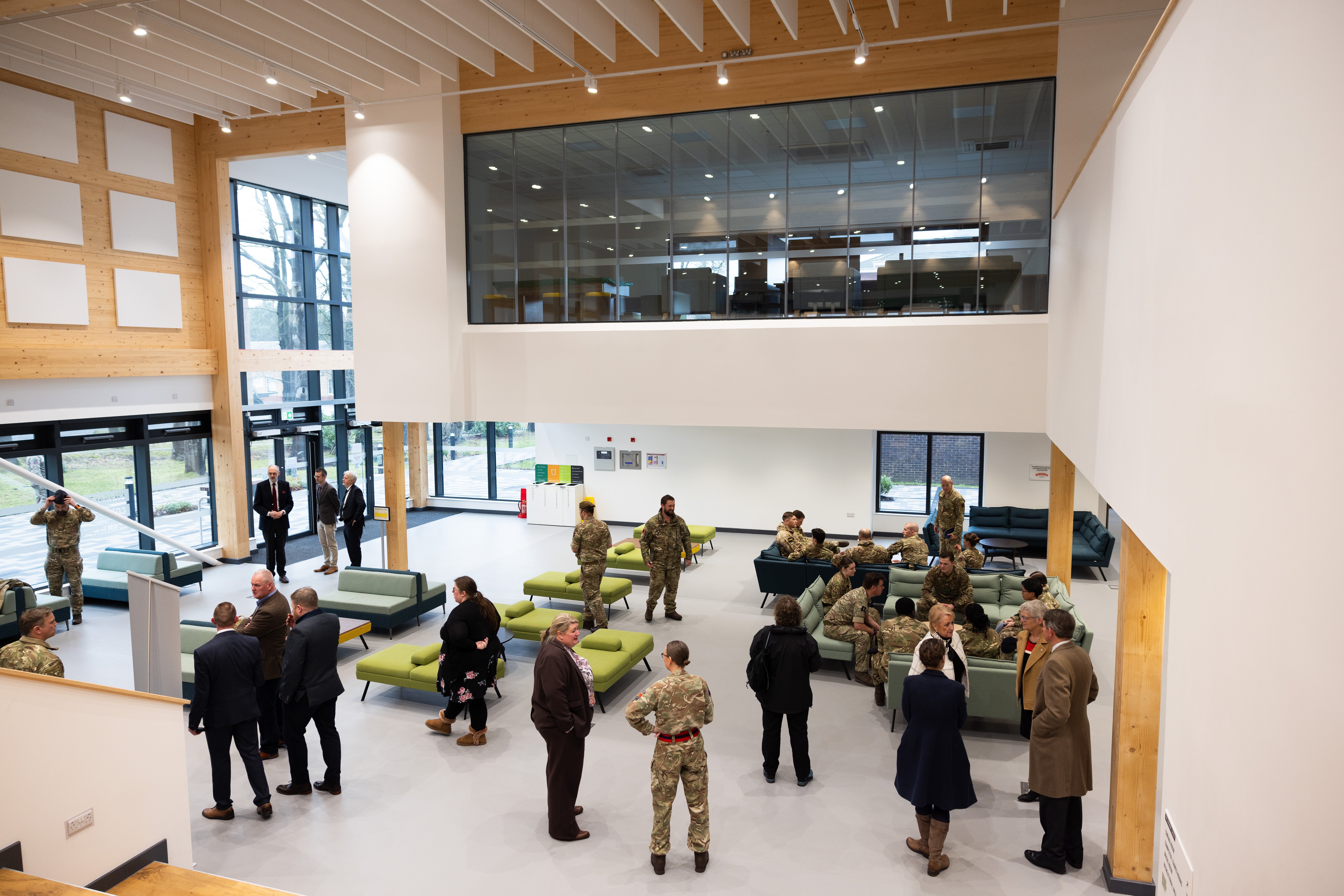 Military and civilian personnel are pictured inside of a modern building. 