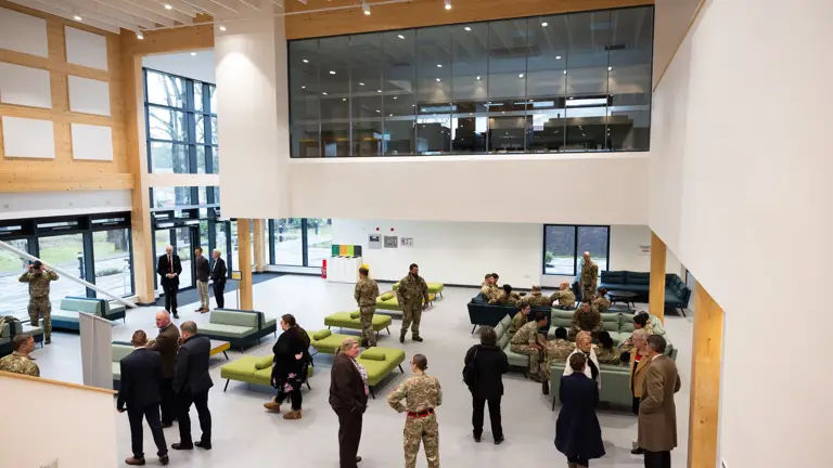 Military and civilian personnel are pictured inside of a modern building.