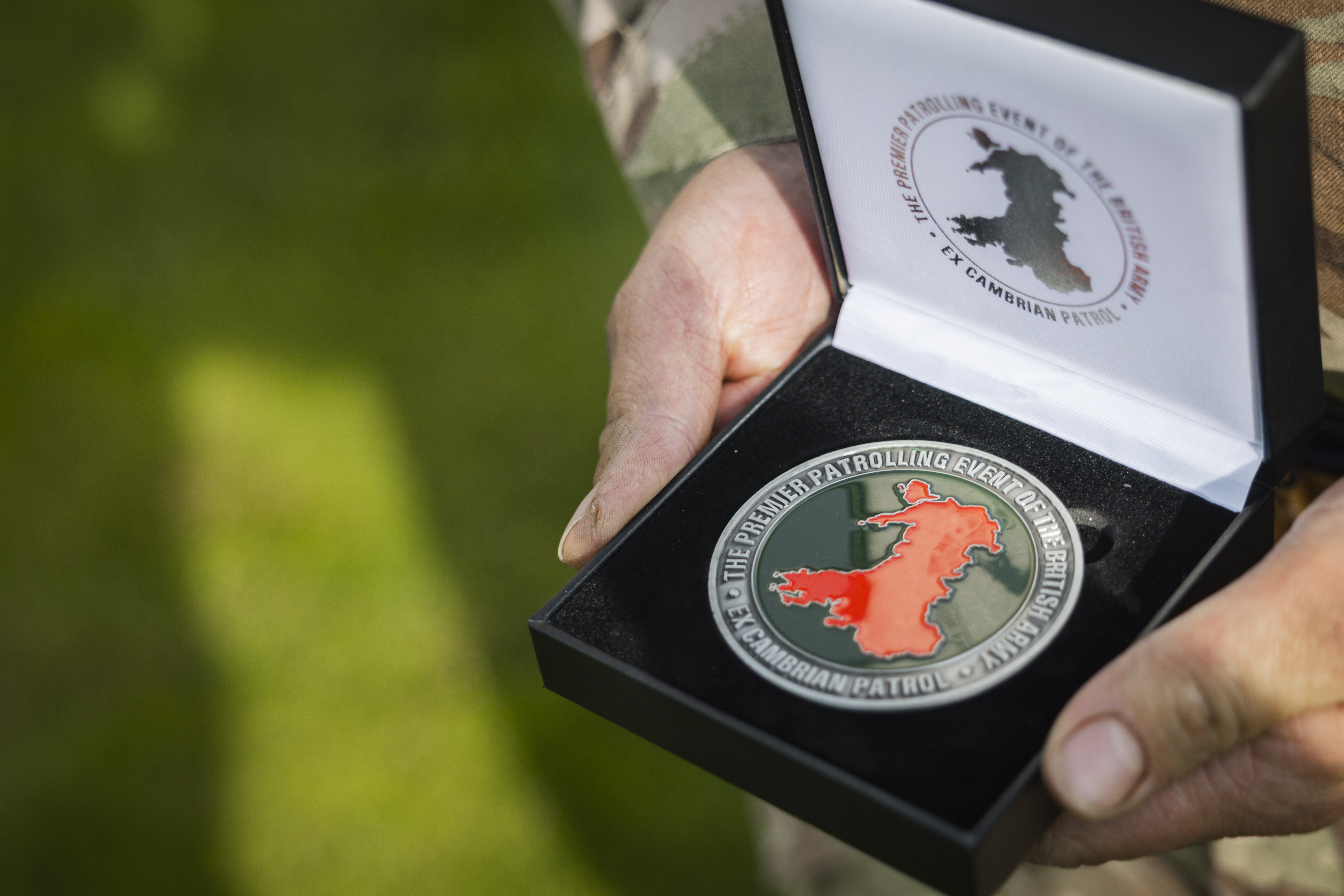 Close-up of hands holding an open black box containing a commemorative medal with a red map of Wales.