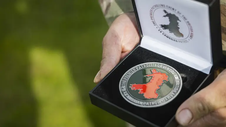 Close-up of hands holding an open black box containing a commemorative medal with a red map of Wales.