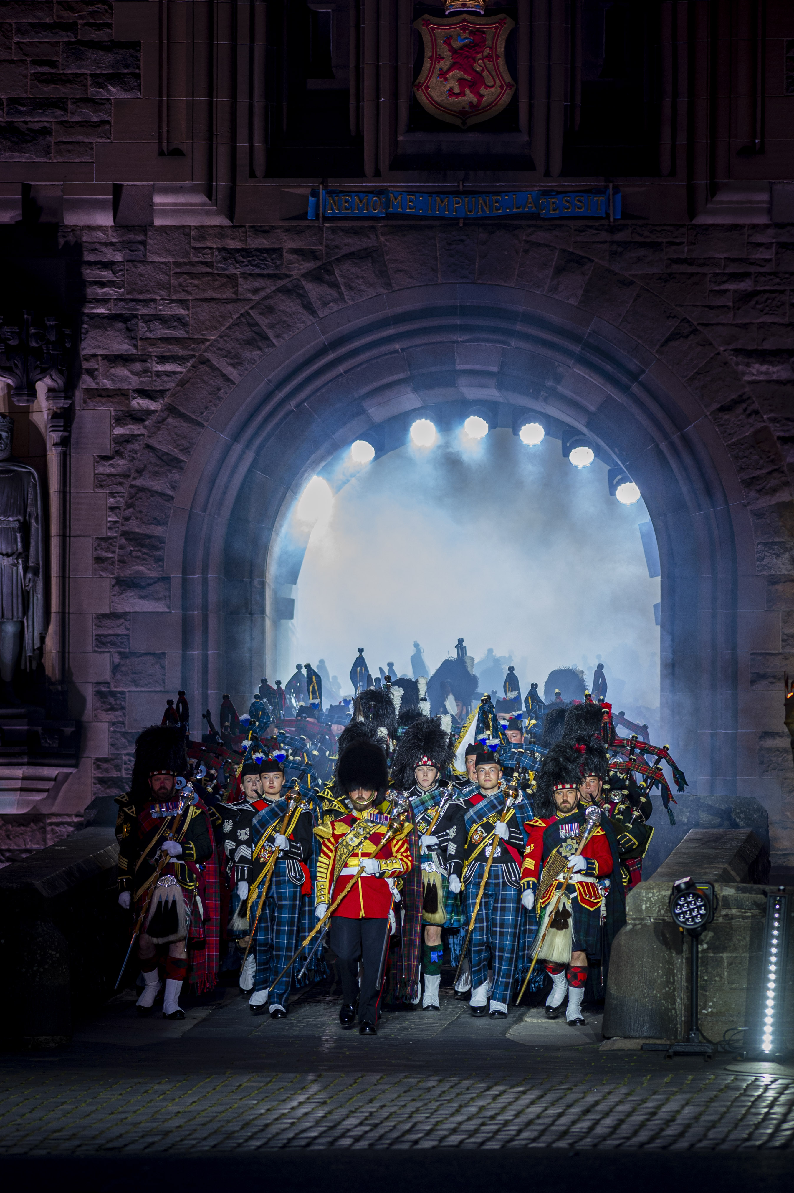 Massed Pipes and Drums makes their entrance through an archway at the Edinburgh castle. The archway is lighting then as the walk through as it is dark outside.