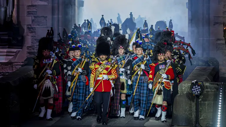 Massed Pipes and Drums makes their entrance through an archway at the Edinburgh castle. The archway is lighting then as the walk through as it is dark outside.