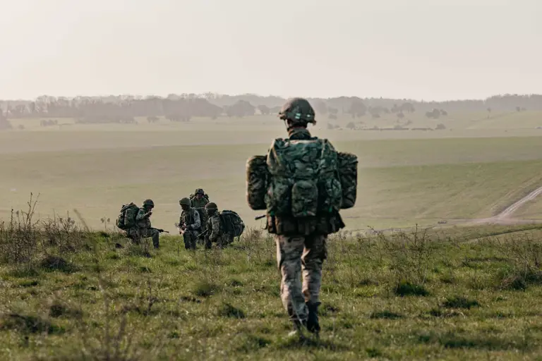 Several individuals in camouflage gear and helmets are walking across a grassy field.