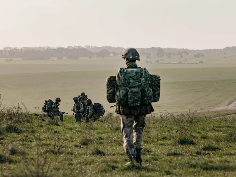 Several individuals in camouflage gear and helmets are walking across a grassy field.