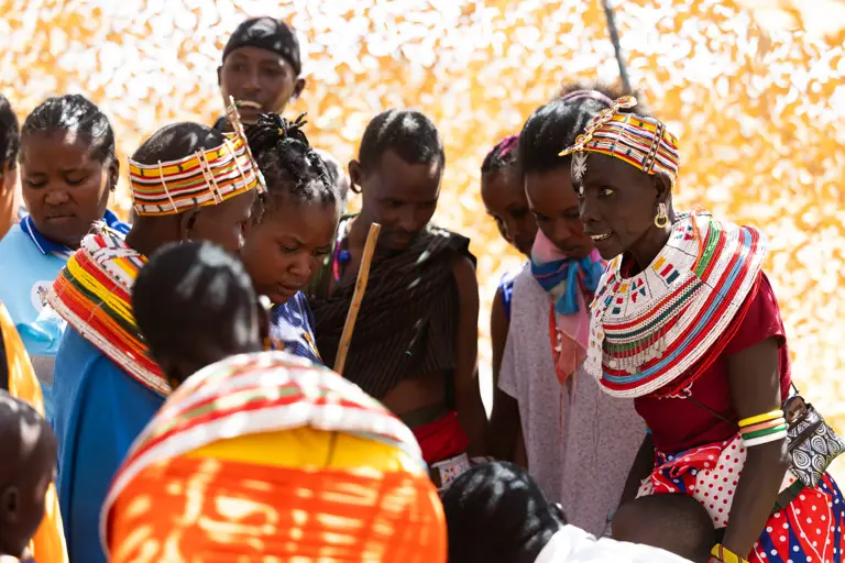 A group of Kenyan locals are pictured, some are wearing bright and multi-coloured clothing. 