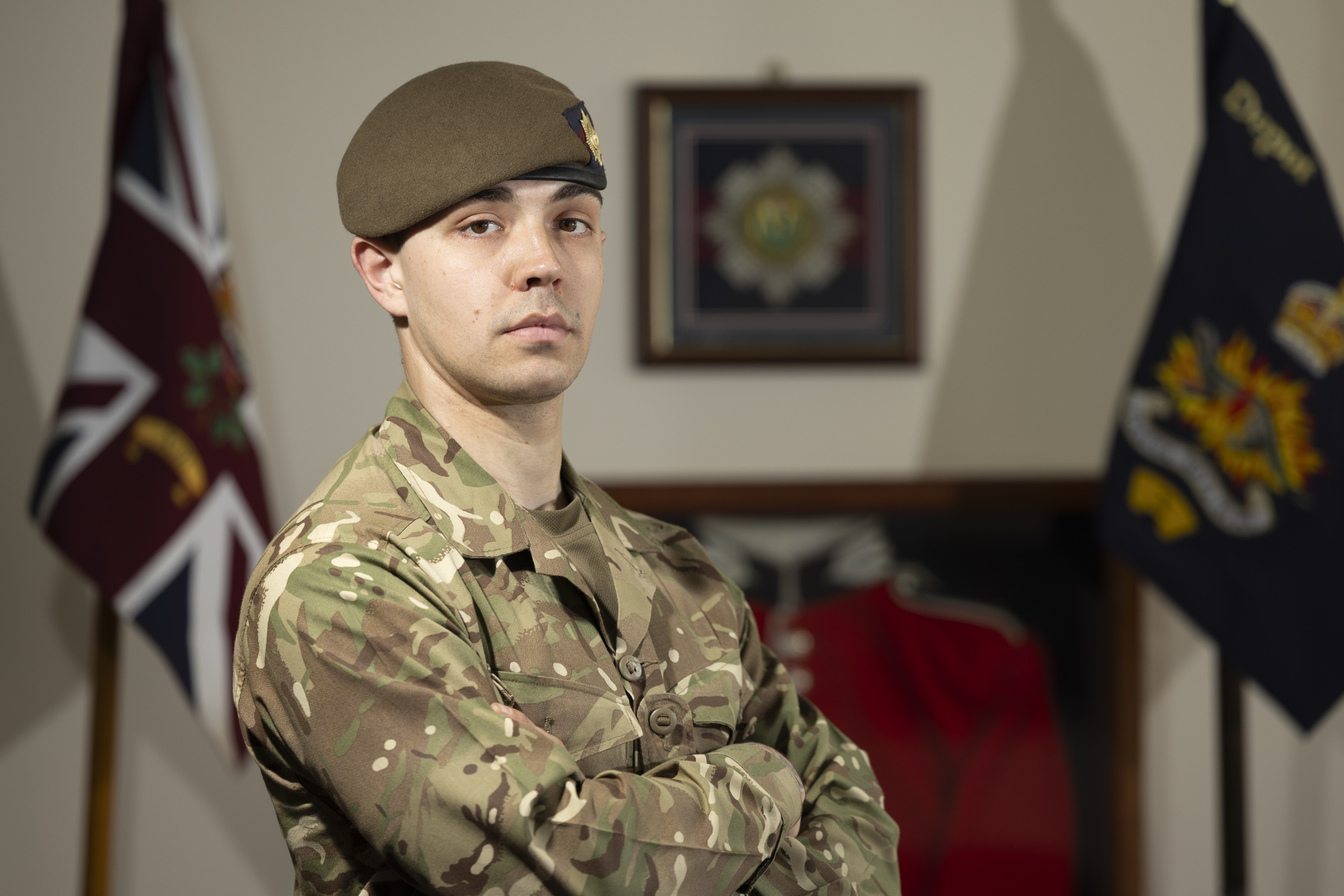 Guardsman stood posing in his camouflage uniform with beret on showing a coldstream guards cap badge.