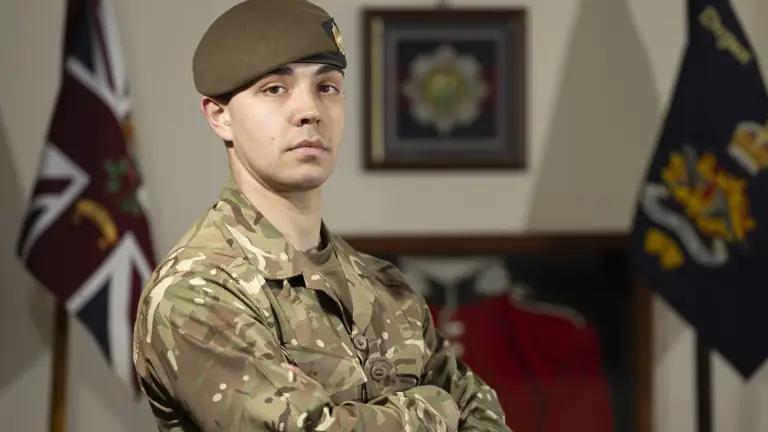 Guardsman stood posing in his camouflage uniform with beret on showing a coldstream guards cap badge.