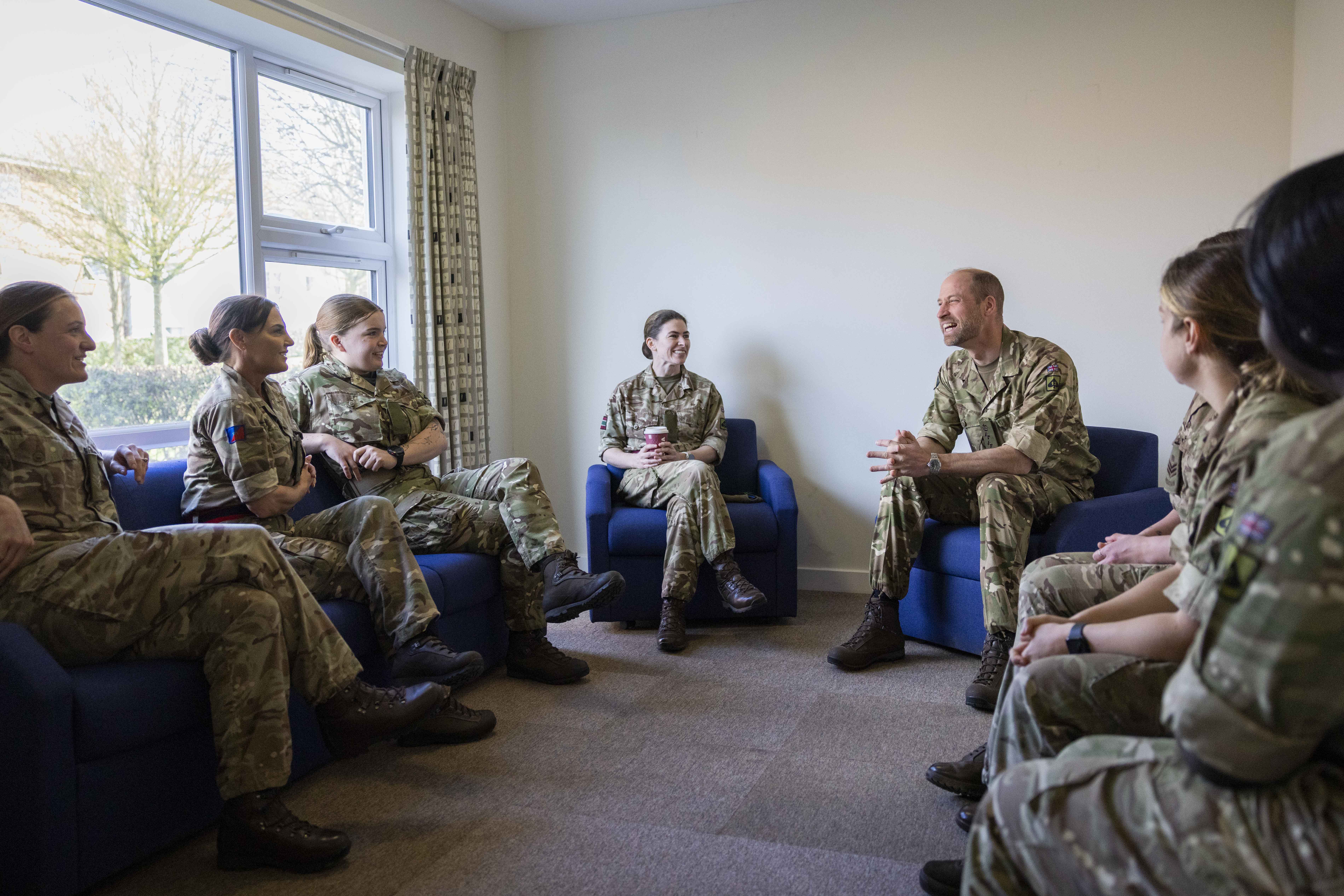 A group of people in military uniforms are seated in a room having a discussion. 