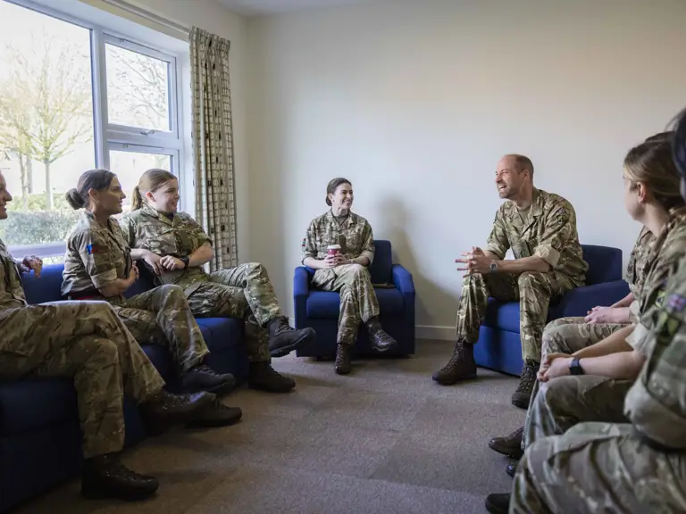 A group of people in military uniforms are seated in a room having a discussion.