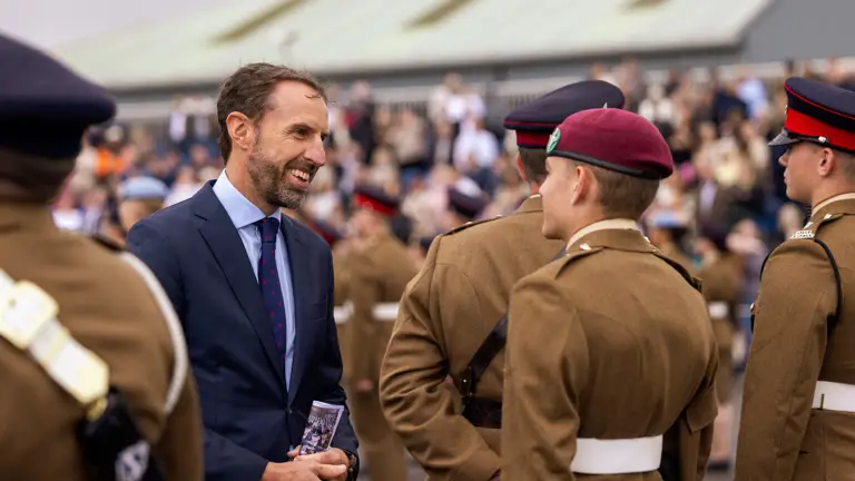Soldiers stood for inspection are seen chatting with Sir Gareth Southgate who is wearing a suit and tie. Family and friends are seen in the crowd in the background.
