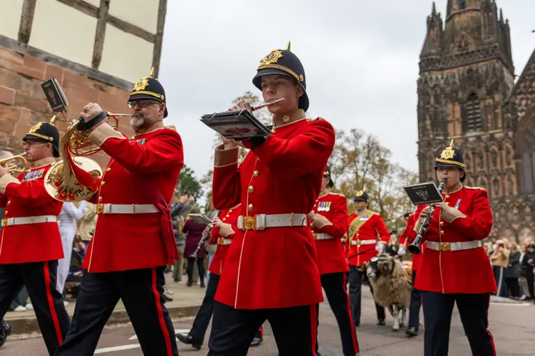 Musician Soldiers wearing their red uniform marching in front of the cathedral playing their instruments.    