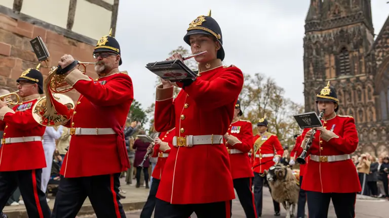 Musician Soldiers wearing their red uniform marching in front of the cathedral playing their instruments.