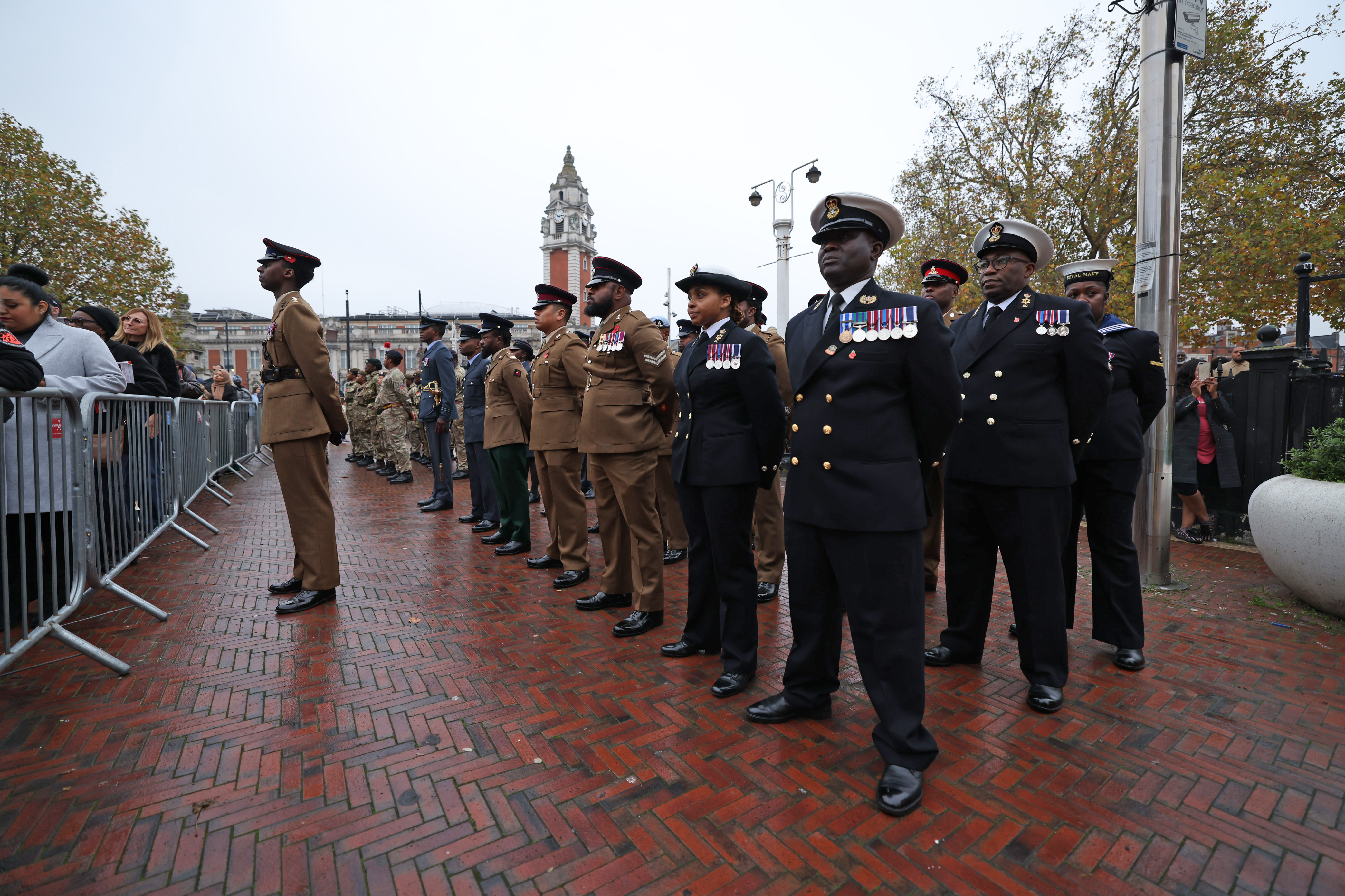 Soldiers, sailors and airmen stand in ceremonial uniforms on a parade.