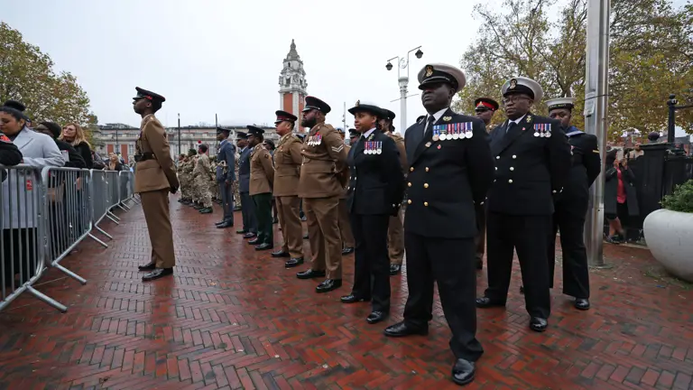 Soldiers, sailors and airmen stand in ceremonial uniforms on a parade.