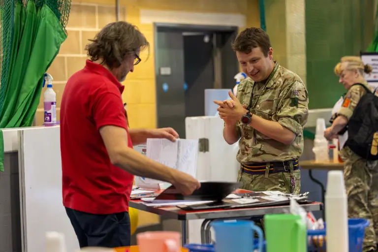 A man in a red shirt reviews documents while a soldier in camouflage listens attentively indoors.