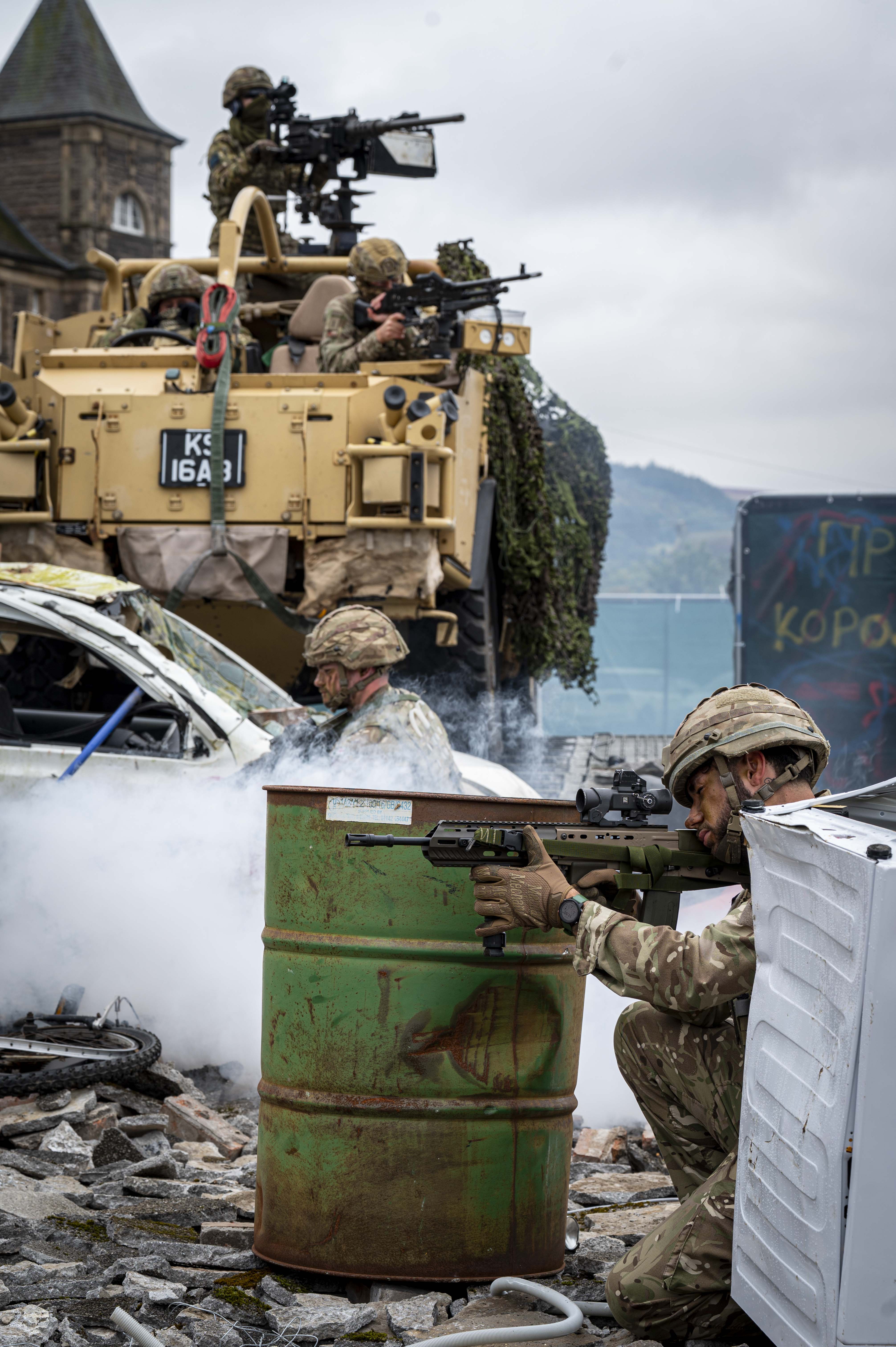 Soldiers shown demonstrate an attack scenario outside with debris including a child's swing, a car and white goods and a jackal with Soldiers in coming through the back.