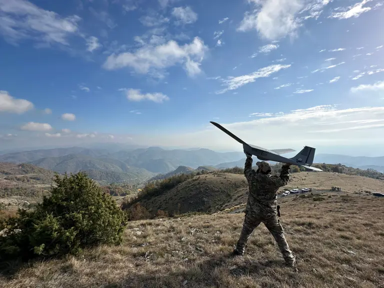 A soldier stands on top of a hill about to throw a drone.