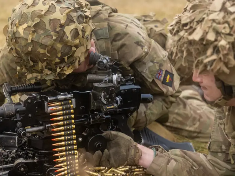 Two soldiers lay next to a machine gun preparing to fire.