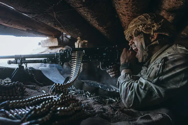 Soldier in a bunker screaming while shooting a machine gun while wearing camouflage and a helmet.