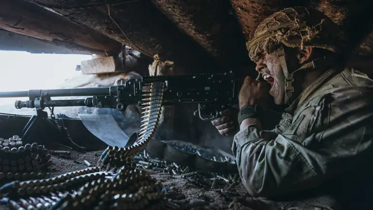 Soldier in a bunker screaming while shooting a machine gun while wearing camouflage and a helmet.