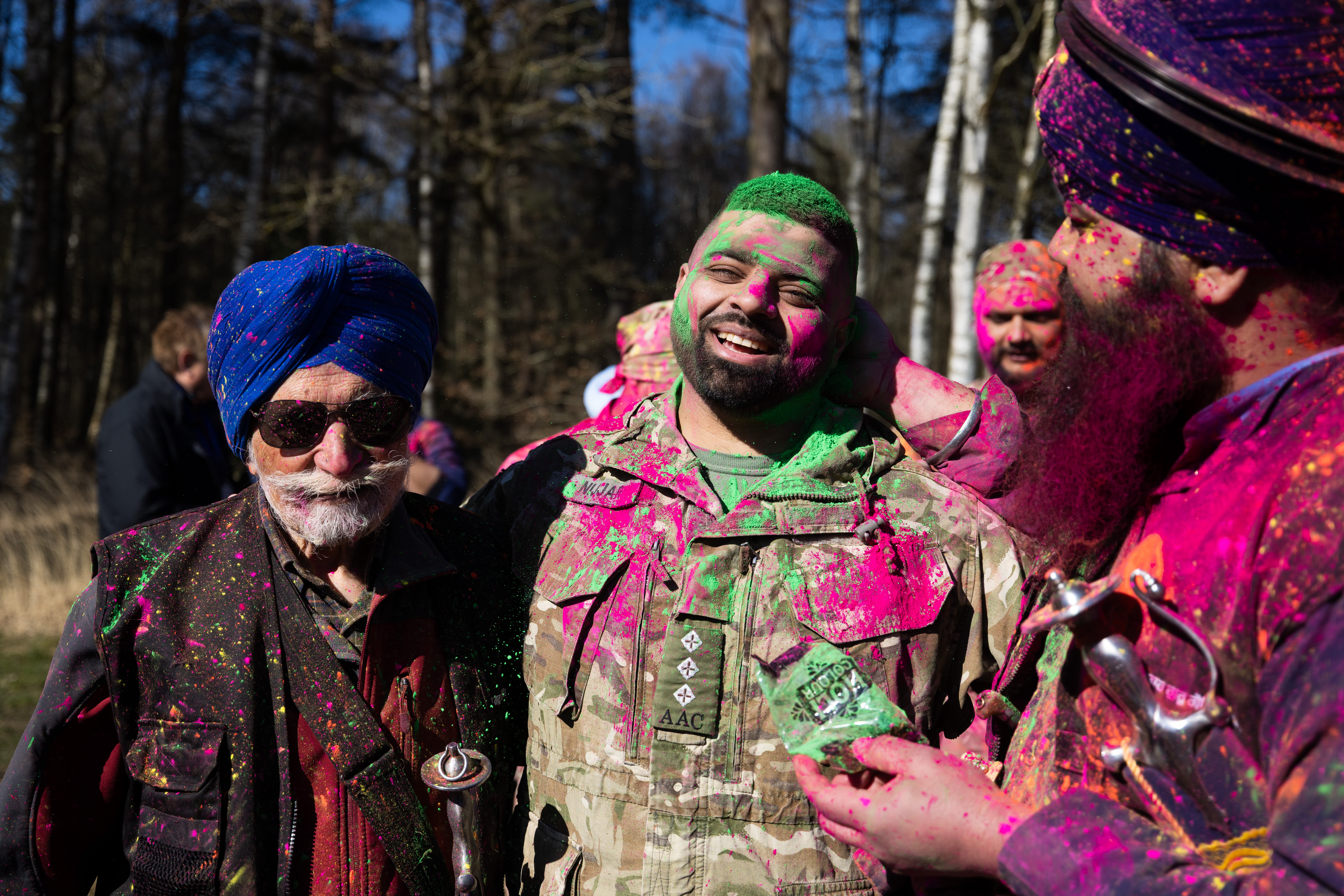 Three Sikh men are pictured covered in neon powder, the man in the middle is wearing British Army uniform. 