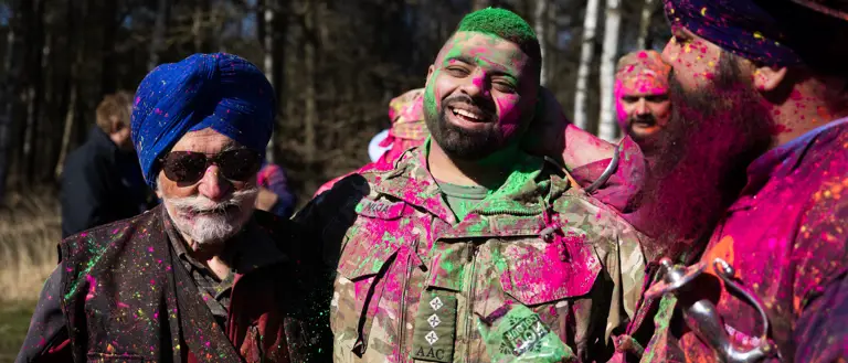 Three Sikh men are pictured covered in neon powder, the man in the middle is wearing British Army uniform.
